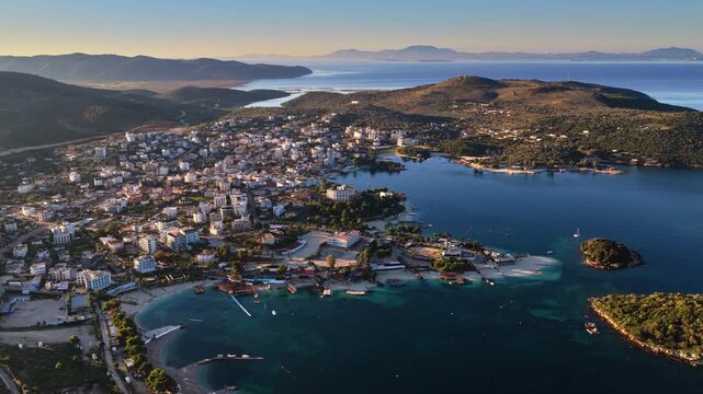 Aerial drone view of Ksamil town, it's dense cluster of hotels and houses, and the iconic bright blue bays with floating platforms and beach clubs