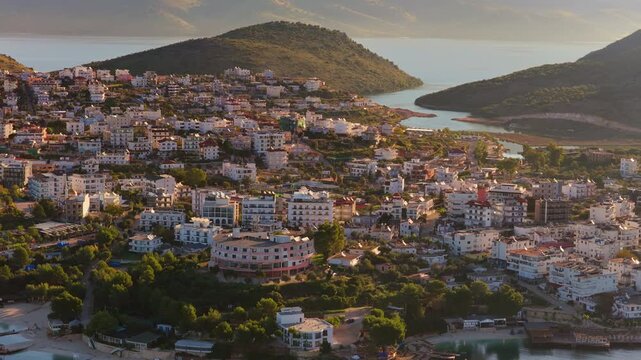 Aerial drone view of Ksamil's hilltop neighborhoods, with layered houses overlooking small coves and forested patches leading to the sea