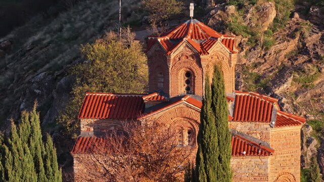 Aerial drone view of the iconic St. John the Theologian Church perched above Lake Ohrid, framed by cypress trees and autumn colors. North Macedonia