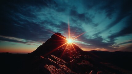 Dramatic sunset rays illuminate the rocky summit of a mountain against a dark blue sky