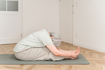 Stretching in the room, senior woman with gray hair doing flexibility exercises