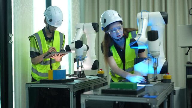 Professional engineering team testing collaborative robots. Female specialist inspecting automated machinery while colleague uses tablet to calibrate systems in a modern smart factory.
