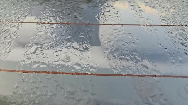 Close-up shot of water droplets and condensation on a car's rear windshield during a rainy day. The orange defroster heating lines are visible through the glass, creating a rhythmic pattern. Perfect f