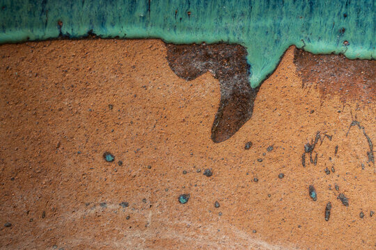 Macro shot of green glaze dripping over a rough terracotta pottery surface, creating a unique and artistic handcrafted texture background