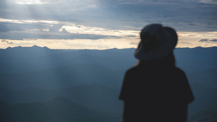 Fototapeta premium Blurred rear view of a woman watching sunset sky on the mountain peak