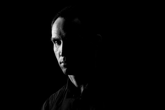 Close-up of a dramatic portrait of a mature serious guy, a musician, singer, rapper in black clothes . half a face on a black isolated background