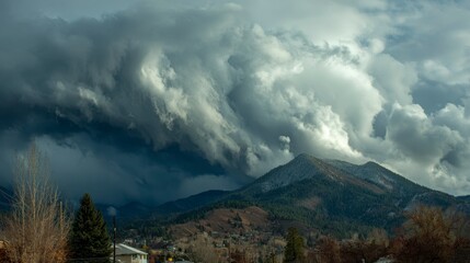 Dramatic panoramic view of mountains obscured by billowing storm clouds with a town nestled at their base