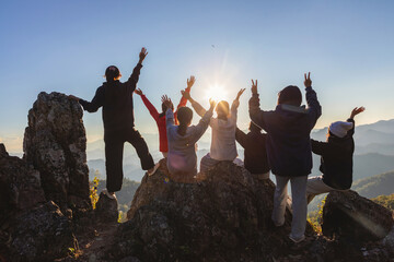 Groups of young people happily raising their hands on top of rocky mountain