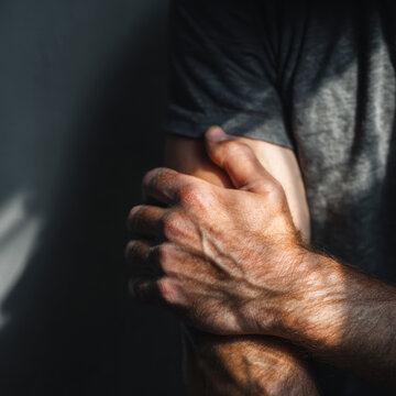 Close-up of a Caucasian adult man gripping his own arm, showing tension, stress, and emotional restraint through raw human body language and physical gesture.