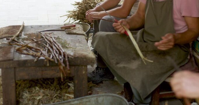 Group of craftspeople manually processing plant fibers and wooden branches in a rustic workshop. This collaborative handmade process demonstrates traditional papermaking and artisan production techniq