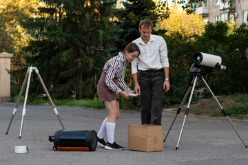 A student selects telescope equipment parts from a box while her teacher observes, during a practical astronomy session focused on science, teamwork, and discovery