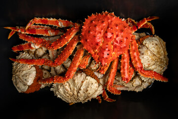 A vibrant red freshly cooked king crab rests with its spiny legs extended across other crabs, showing detailed marine textures and seafood presentation
