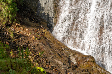 A rushing waterfall flows over rocks at its base, creating foam and spray