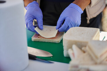 Blue Gloved Hands Assemble Ham and Cheese Sandwich on Fresh Bread at Deli Station