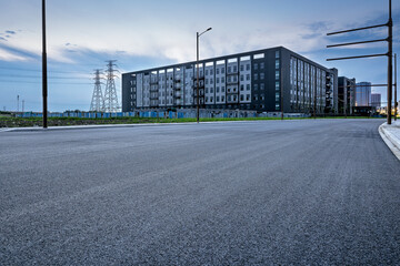 Obraz premium Empty asphalt road leading to a modern building with power lines in the background.