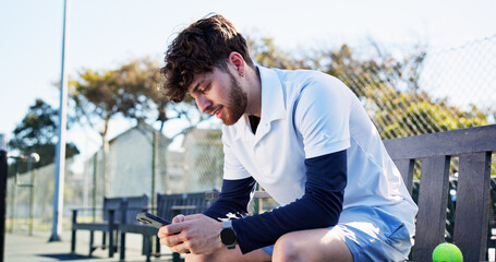 Athlete, man and relax with phone on tennis court for fitness, training app and match progress. Happy, male person and mobile on bench for sports break, video demonstration and online results of game
