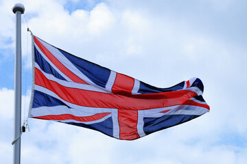 The British Union Jack flag flutters powerfully in the wind under a blue sky