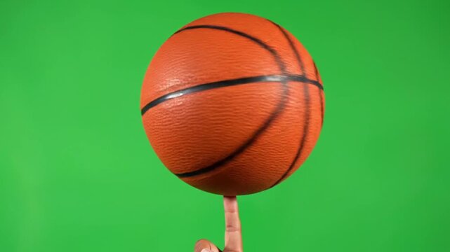 Close up of a person expertly spinning an orange basketball on one finger against a green screen background
