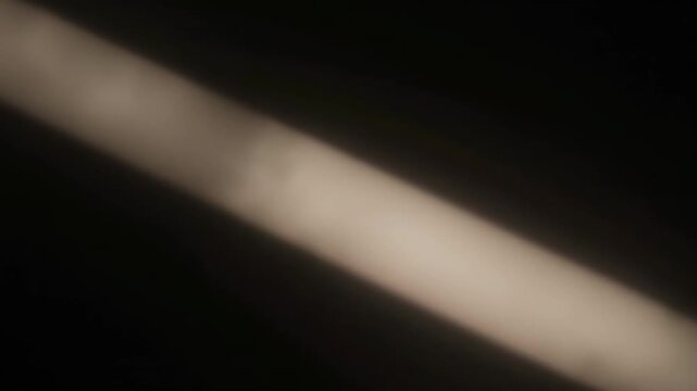 A blurry diagonal band of muted light cuts across a dark background creating a contrast