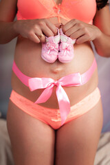 A pregnant girl with a bow on her stomach holds children's socks.