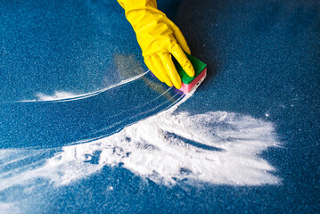 a hand in a yellow rubber glove washes a wall with a wet foamy blue sponge, foam blue background copy space, cleaning concept, household chores, spring cleaning