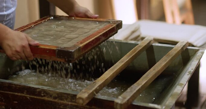 Fresh handmade paper sheets placed on a wooden press and drying surface inside a traditional workshop. This scene illustrates the manual papermaking process using natural fibers and simple tools.