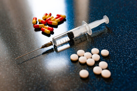 A lot of pills in a heart shape and syringe with injection on a blue background as a symbol of medical treatment. Choice antibiotics against vaccine from Covid-19. Emergency help in case heart attack