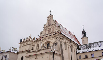 Poland, St. Joseph Church, Lublin. A historical church stands in a small town with snow on its rooftop. The scene takes place in winter with cloudy skies. Details of the church