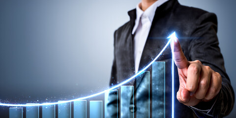 A businessman points towards a successful upward trending bar graph representing financial growth and strategy.