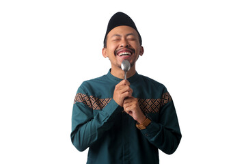 Asian Muslim man wearing a black peci cap (songkok), licking a spoon with a thoughtful expression...