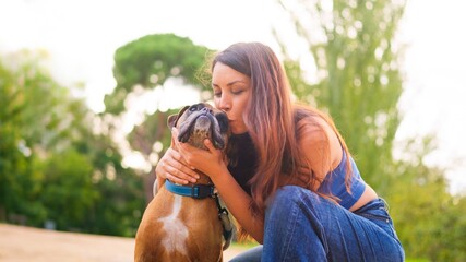 Woman embracing and kissing boxer dog in a park