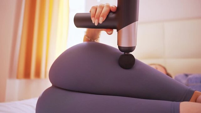 Woman pressing massage gun on Hip in tight leggings with a close low angle showing slow motion Thigh ripple under vibration