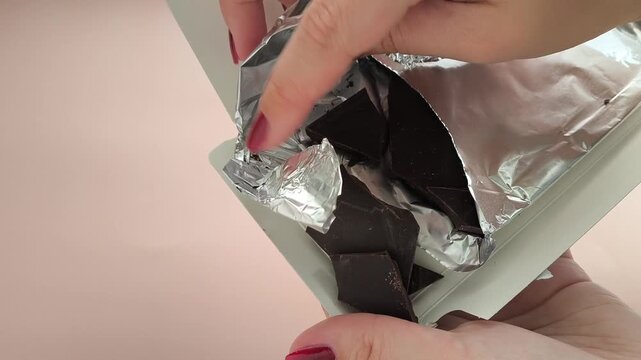 Female hands opening chocolate in foil. Natural dark chocolate from cocoa beans