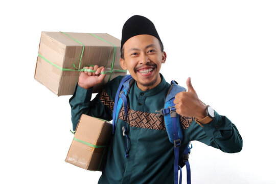 Excited Asian Muslim man holding cardboard boxes, and showing a thumbs-up gesture, ready for mudik, the Indonesian tradition of to visit family and celebrate Eid Mubarak, Isolated on white background