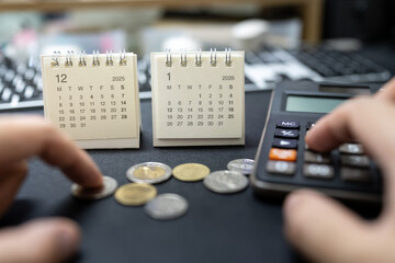 Person using calculator with coins and calendars for 2025 and 2026 representing financial struggle and budget crisis. Economic recession, inflation impact, lack of savings, and financial stress.