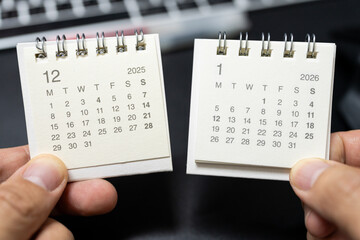 Hands holding desk calendars showing December 2025 and January 2026 for New Year transition concept.