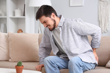Young man with hemorrhoids and cactus sitting on sofa at home