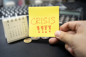 Hand holding sticky note with CRISIS text and 2026 calendar for economic warning concept. upcoming financial global crisis, economic downturn, inflation alerts.