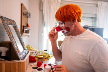 Man preparing for clown performance with makeup and wig