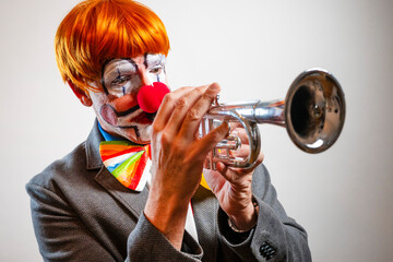 Sad clown playing trumpet in costume with creative makeup