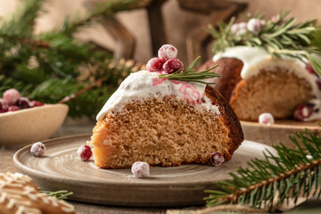 A piece of Christmas gingerbread cake with white sugar glaze decorated with cranberries on a plate, wooden festive rustic decorated background