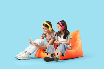 Obraz premium Cute Asian sisters in headphones with tablet computer watching cartoons on blue background