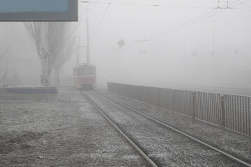 A red retro tram traverses silence street in foggy morning