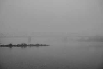 Fototapeta premium Nebel über dem Fluss und einer Brücke in einer Stadt am Abend