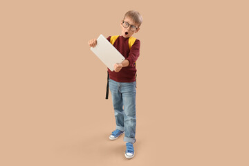 Shocked little schoolboy with tablet computer on beige background