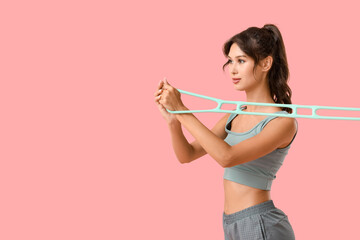 Sporty young woman exercising with fitness expander on pink background
