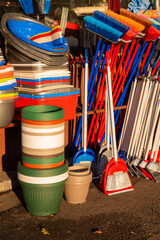 A storefront display outside a shop featuring various plastic housewares: dishes, brooms, dustpans, and other household cleaning items.

