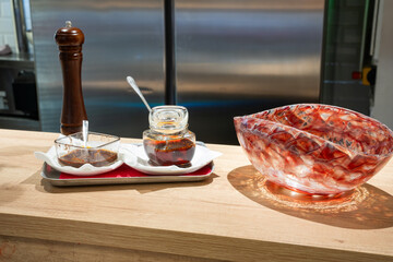 Two glass bowls with sauces on a serving tray, accompanied by a pepper grinder and a decorative glass dish. A restaurant table setting arrangement.


