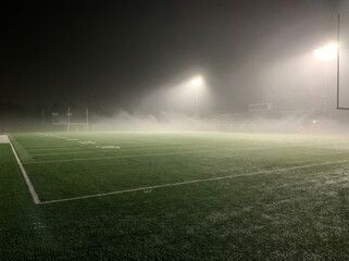 Obraz premium American football field at night illuminated by stadium lights through thick fog.