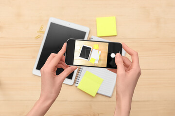 Female photographer taking picture of tablet computer with stationery on wooden background, top view